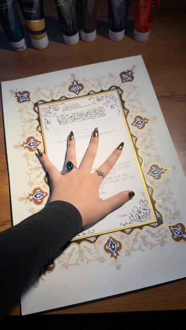 A hand resting on a hand-painted Nikkah Nama with a jewel-toned Mughal border