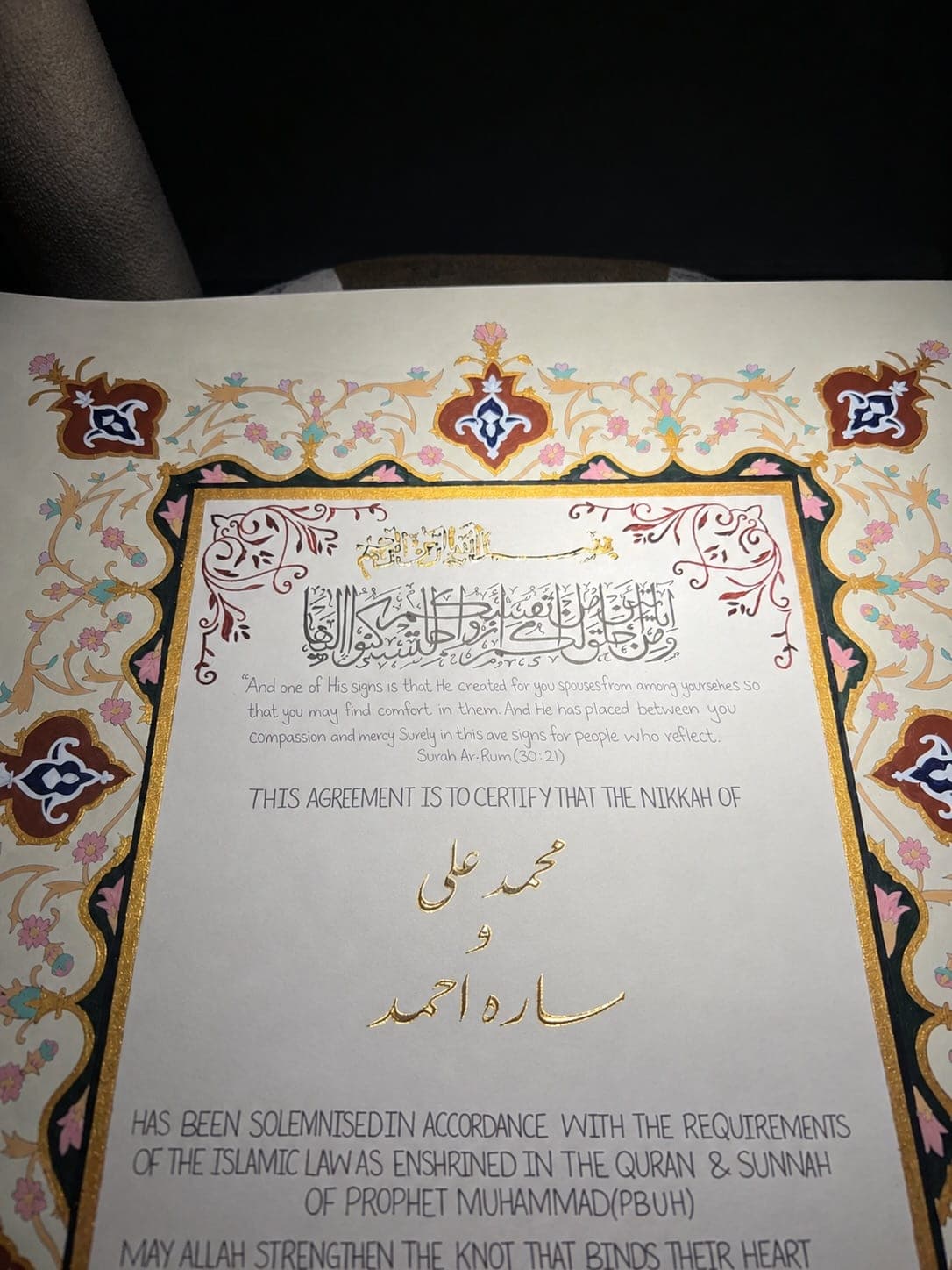 Close-up of a Nikkah Nama with Urdu names written in gold inside a painted floral border