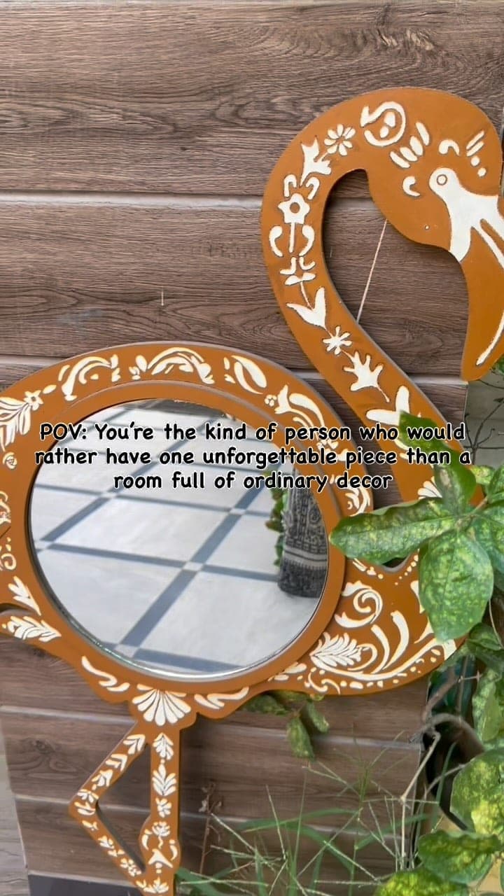 Flamingo-shaped mirror in burnt orange with white folk patterns, beside a plant