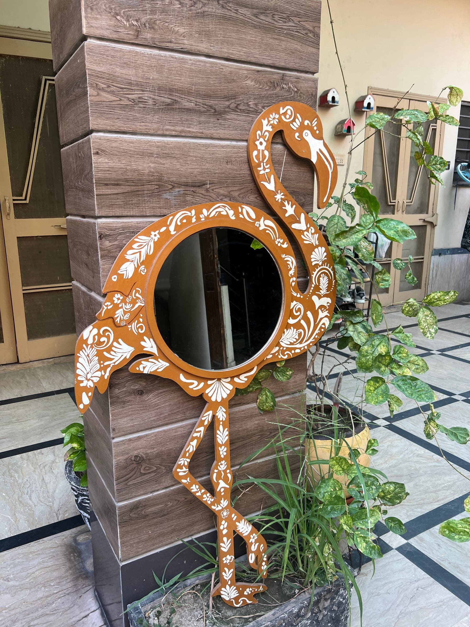 Close view of the Flamingo Mirror against a wood-clad pillar, showing the hand-painted white patterns