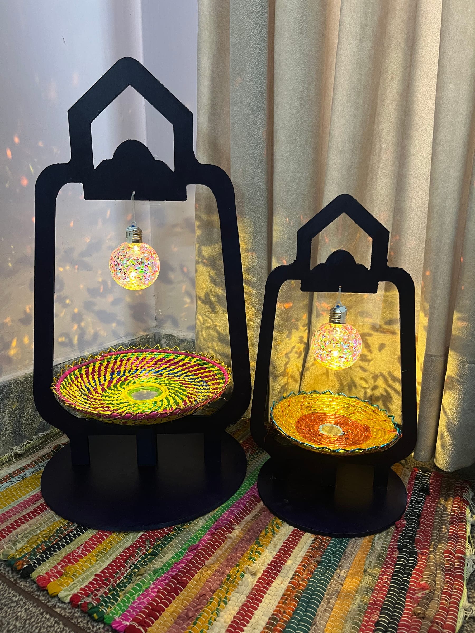 Two navy lantern gift stands lit from inside, with woven trays and glowing bulbs