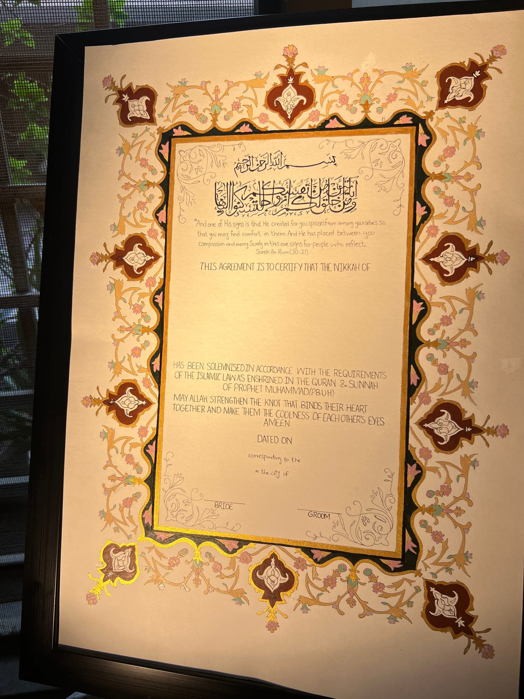 A framed Nikkah Nama in warm lamplight, the gold border glowing around the certificate