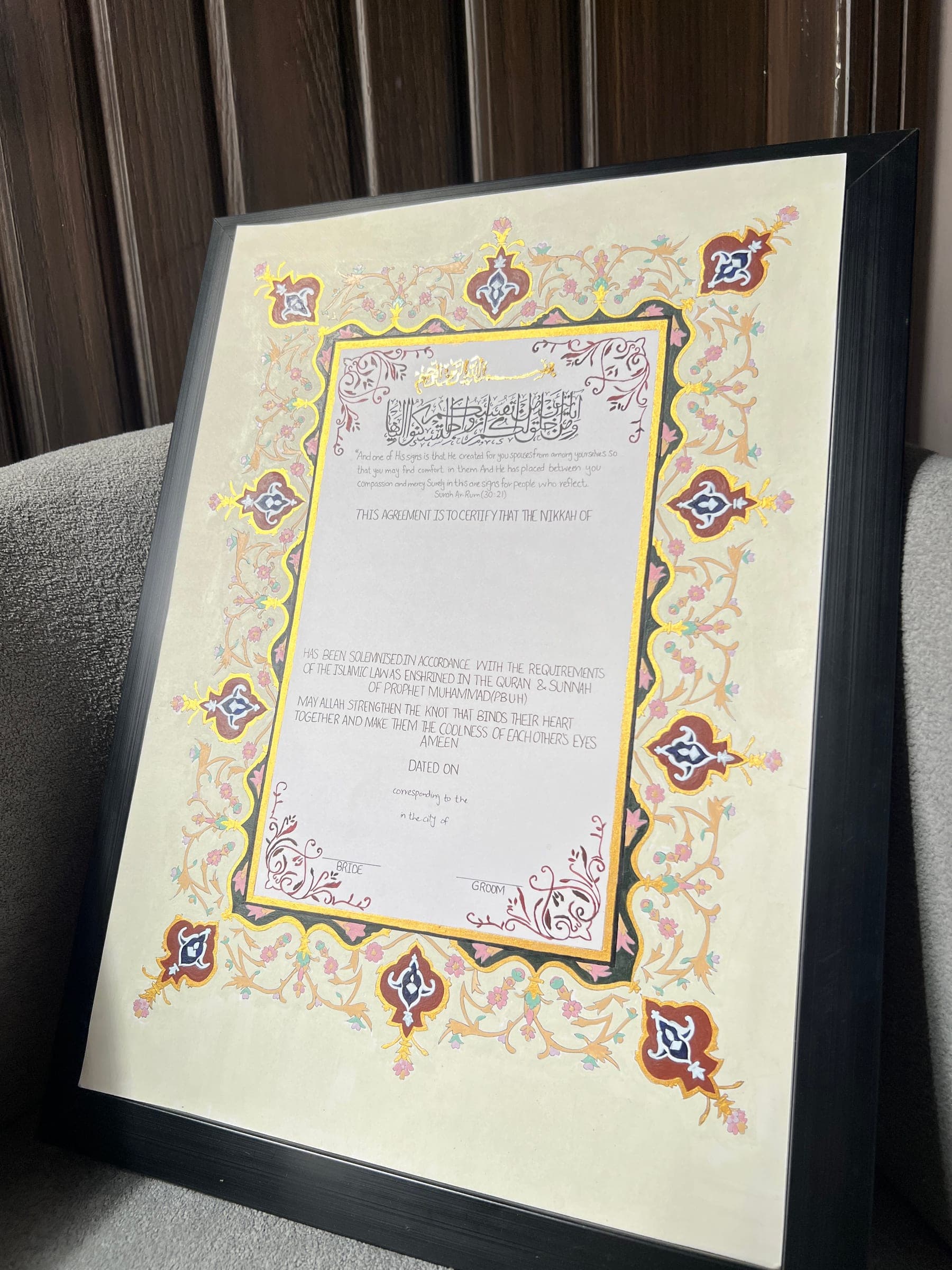 An illuminated Nikkah Nama finished in a slim black frame, leaning against a wall