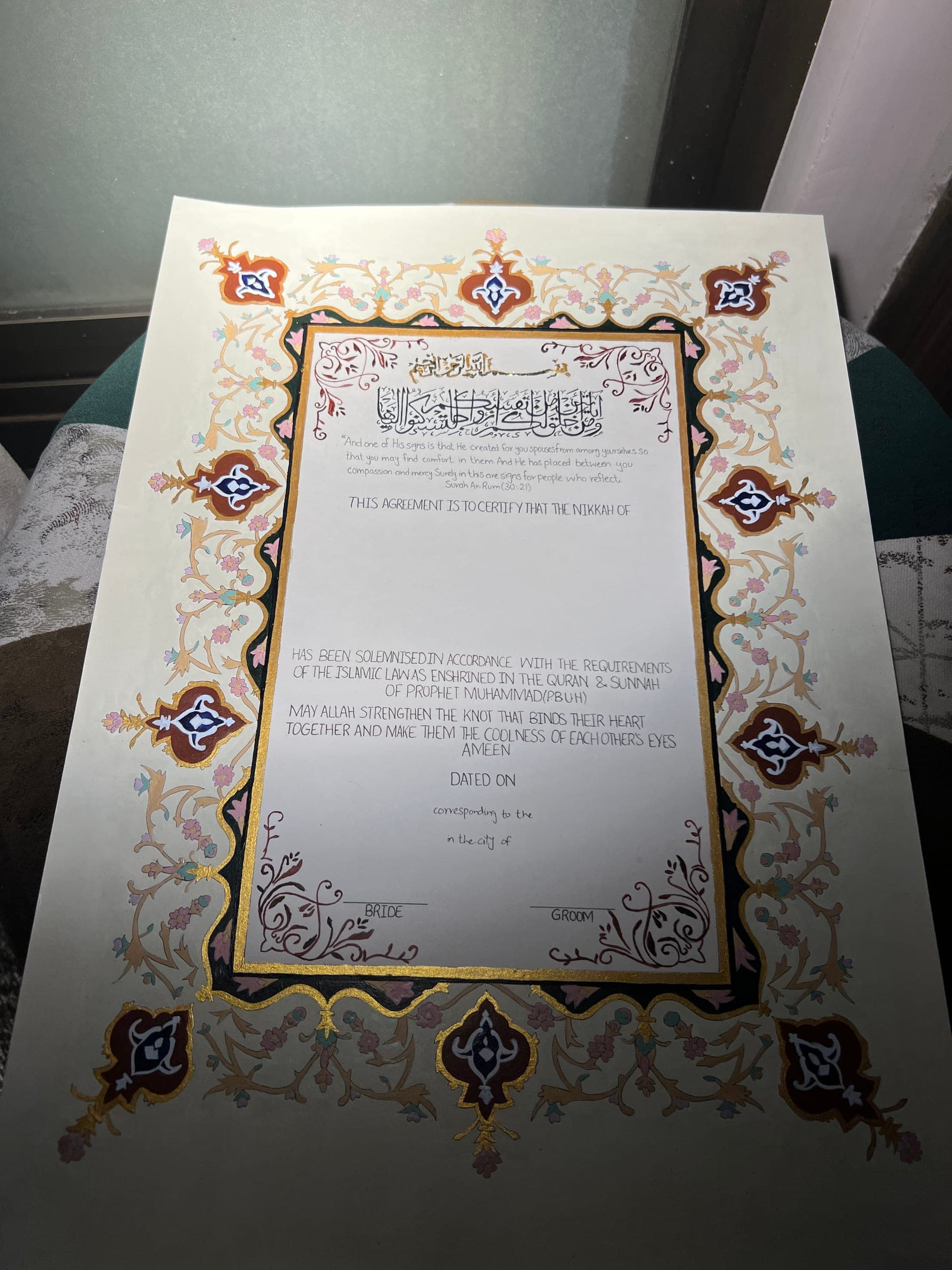 A Nikkah Nama seen at an angle, showing the gilded inner frame and the hand-lettered ayah at the head