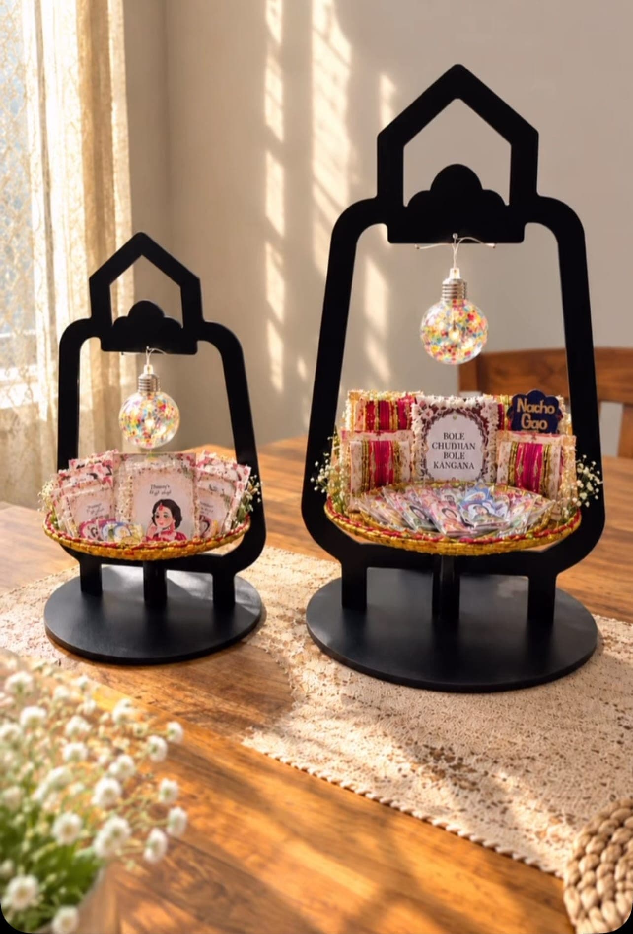 Two black lantern-shaped gift stands holding mehndi favours, lit by glowing bulbs