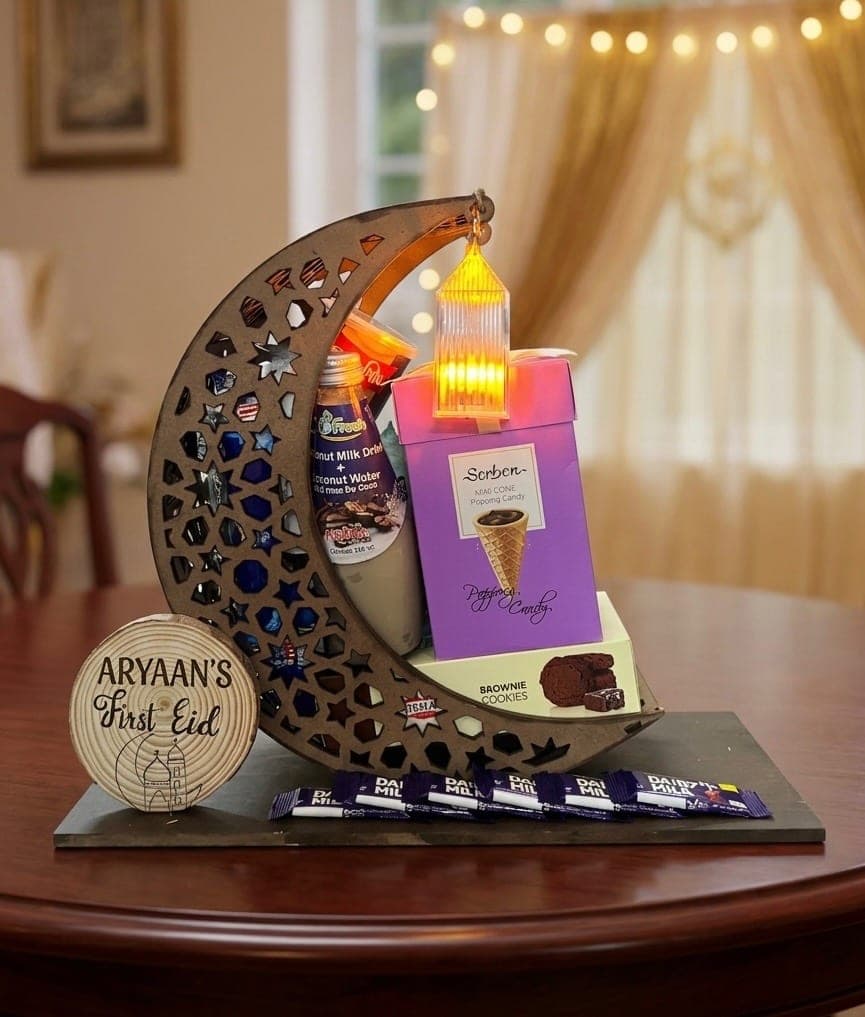 The crescent moon tray lit up on a dining table, filled with sweets and a personalised First Eid disc