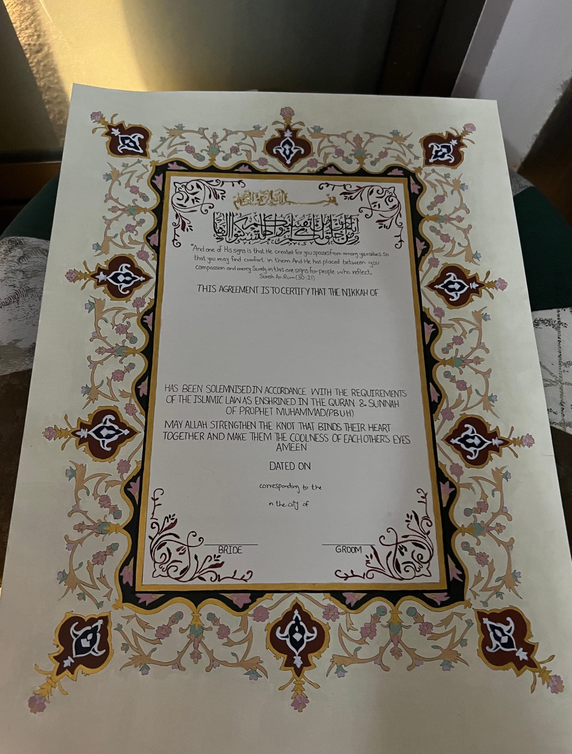 The full painted border of a Nikkah Nama laid flat, with burgundy and navy cartouches at each corner and edge