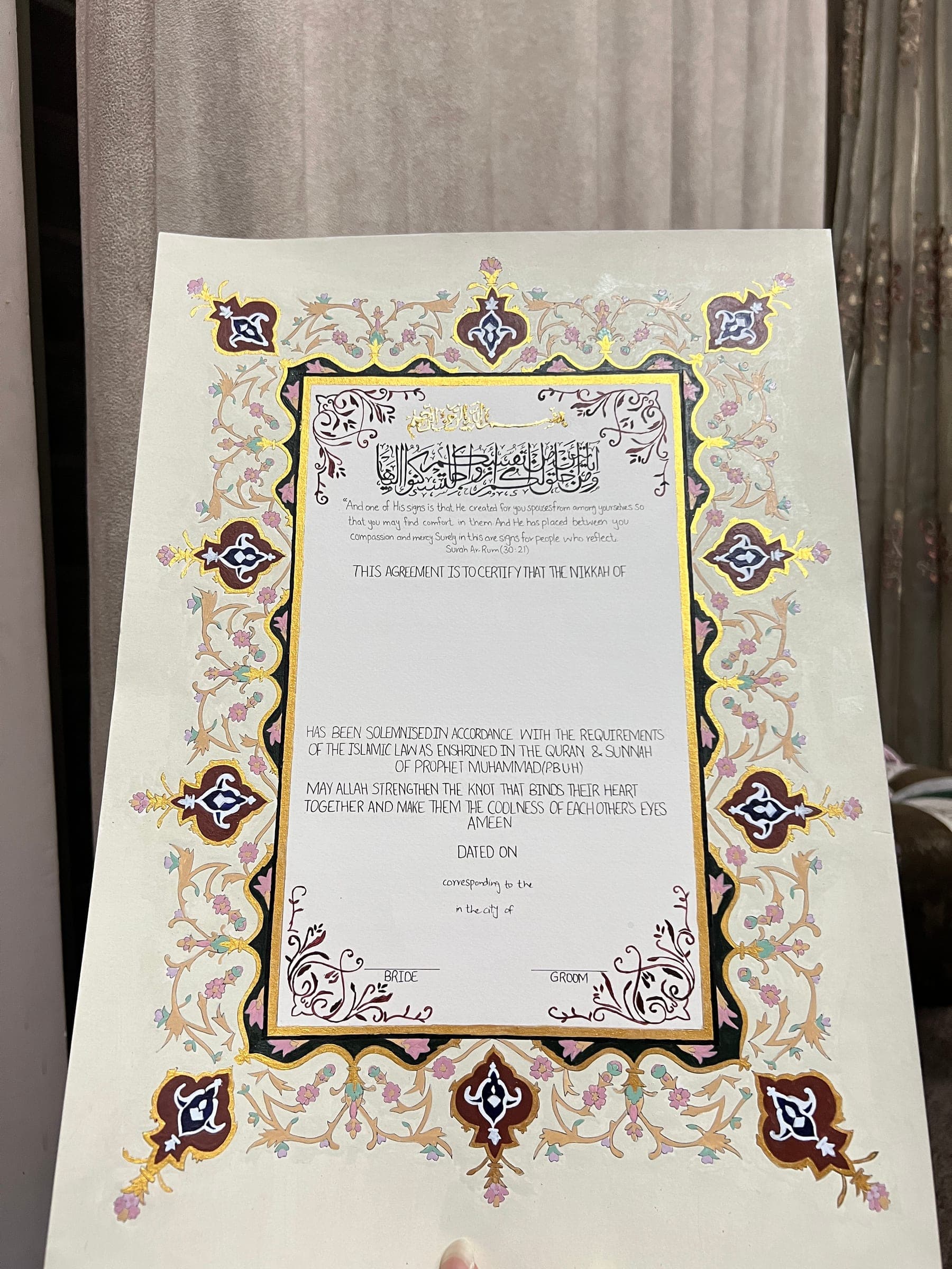 A finished Nikkah Nama propped upright, its gold frame catching the light inside a painted floral border