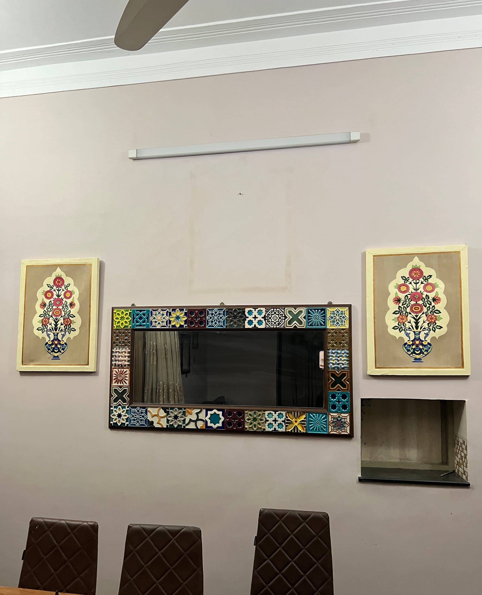 Two Mughal floral canvases hung either side of a tile mosaic mirror on a pale wall